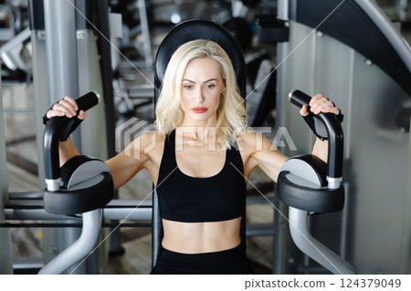 Determined sportswoman exercising using gym equipment for chest muscles 124379049