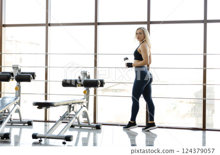 Athletic woman holding water bottle posing in a gym Athletic woman holding water bottle posing in a gym 124379057