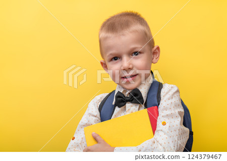 Back to school. A blond funny boy with a backpack in a light shirt on a yellow background holds books in his hands and looks at the camera. Back to school. A blond funny boy with a backpack in a light shirt on a yellow background holds books in his hands and looks at the camera. 124379467