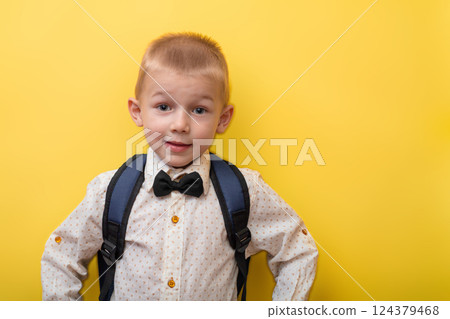 Back to school. A blond funny boy with a backpack in a light shirt on a yellow background looks at the camera. Education 124379468