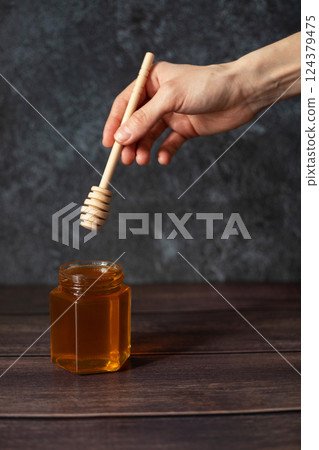 The hand holds a honey stick. A jar of honey. Dark background The hand holds a honey stick. A jar of honey. Dark background 124379475
