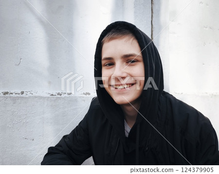 Close-up portrait of young caucasian teenager guy looking at camera smiling. Guy in a black hood outdoors. portrait of a handsome young man 124379905