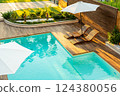 Elegant turquoise swimming pool with wooden deck, lounge chairs, and umbrellas in a sunny backyard 124380056
