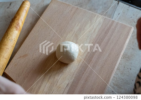 Ball of dough resting on wooden cutting board with rolling pin beside Ball of dough resting on wooden cutting board with rolling pin beside 124380098