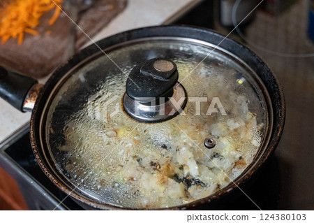 Frying pan with condensation on glass lid simmering onions on stove top 124380103