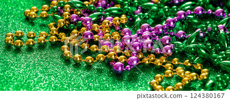 Mardi Gras concept. Multi-colored beads on green shiny background. Fat Tuesday symbol. Festive shining decorations in gold, green and purple colors for traditional holiday. Banner format. Mardi Gras concept. Multi-colored beads on green shiny background. Fat Tuesday symbol. Festive shining decorations in gold, green and purple colors for traditional holiday. Banner format. 124380167