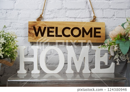 Welcome Home alphabet letters and wooden signboard hanging on white brick wall background 124380946