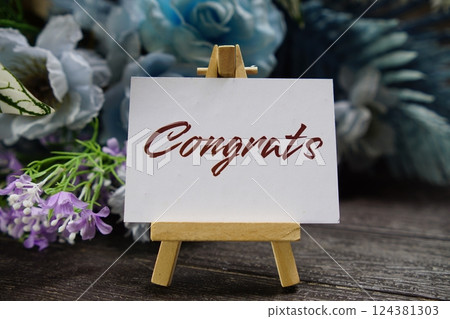 Congrats text write on paper card with wooden easel and flowers decoration on wooden background 124381303