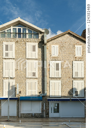 Historic Mediterranean stone building with closed white shutters against a blue sky Historic Mediterranean stone building with closed white shutters against a blue sky 124381469