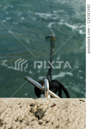 Mooring ring with rope on the waterfront edge in a Mediterranean port Mooring ring with rope on the waterfront edge in a Mediterranean port 124381492
