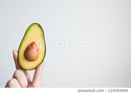 Hand holding halved avocado against minimalist white background 124383000