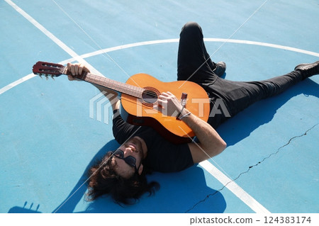 Man Lying On The Ground Plays Classical Guitar On Blue Floor Outdoor Man Lying On The Ground Plays Classical Guitar On Blue Floor Outdoor 124383174