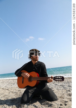 Kneeling Man Plays Guitar Musical Instrument On The Beach Near The Ocean Summer Kneeling Man Plays Guitar Musical Instrument On The Beach Near The Ocean Summer 124383189