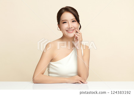 A beautiful young Asian woman with clean, fresh skin against a beige background. Skincare, facial treatment, cosmetology, beauty, and spa. An elegant portrait of an Asian woman. 124383192