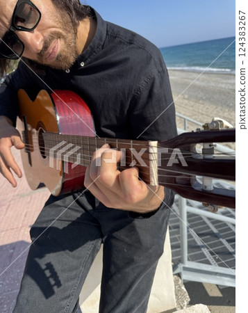 Long Hair Boy Plays Classical Guitar by the Ocean in Summer Dressed in Black Long Hair Boy Plays Classical Guitar by the Ocean in Summer Dressed in Black 124383267