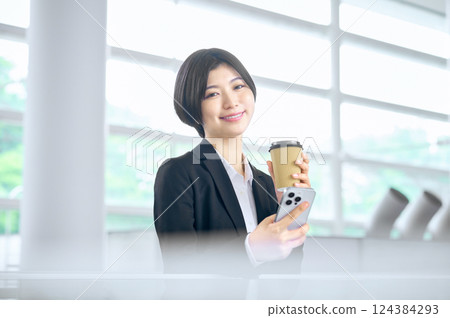 一位身穿西裝的女商人在辦公室裡看著她的智慧型手機 124384293