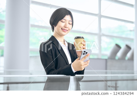 一位身穿西裝的女商人在辦公室裡看著她的智慧型手機 一位身穿西裝的女商人在辦公室裡看著她的智慧型手機 124384294