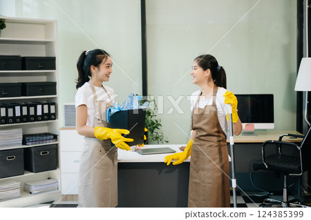 Two professional cleaners tidying a stylish space with a smile. Experience efficient and friendly house cleaning 124385399