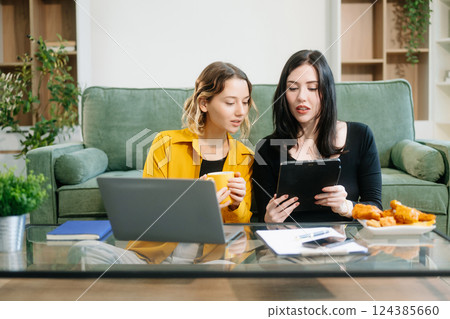 Two cheerful women sitting on a green couch, sharing ideas using a laptop and phone in a stylish home Two cheerful women sitting on a green couch, sharing ideas using a laptop and phone in a stylish home 124385660