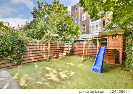 A vibrant backyard features a wooden playhouse, slide, and lush greenery, perfect for children's outdoor activities and relaxation. 124386664