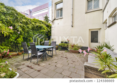 A serene backyard space features a dining table surrounded by green foliage and flowers, ideal for relaxation and outdoor gatherings. A blend of nature and home comfort. 124386669