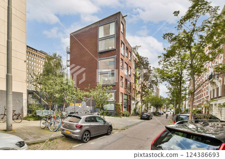 A contemporary residential building stands out with large windows, surrounded by trees and parked bicycles, showcasing urban life in harmony with nature. 124386693