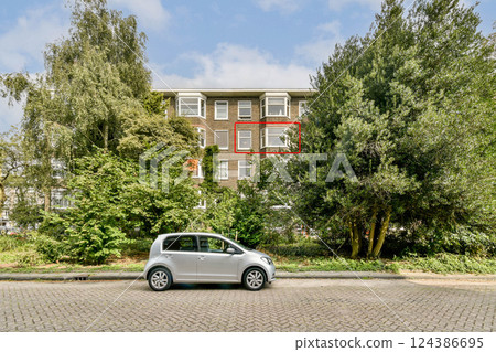 A contemporary building surrounded by lush greenery, showcasing a parked car in the foreground, ideal for urban aesthetics and architecture lovers. 124386695