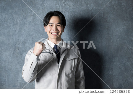 一名身著工作服的男子麵帶微笑，握緊拳頭。建築管理和工廠的工業影像，看著相機。 124386858