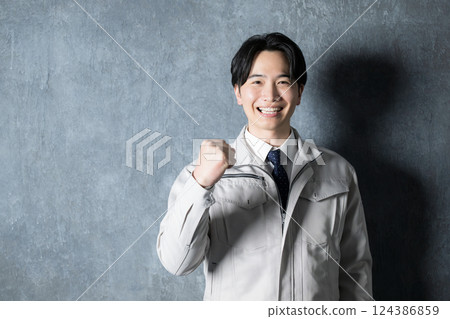 A man in work clothes with a smiling expression making a fist pump. Industrial image of construction management and factories, looking at the camera. 124386859