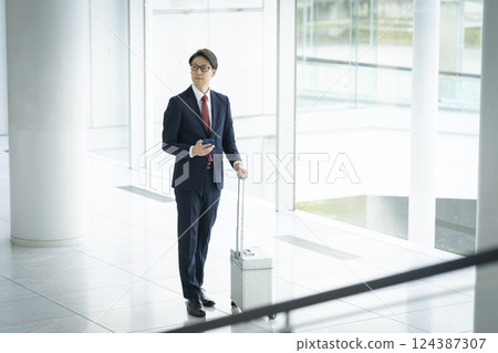 A businessman in his 40s carrying a smartphone and a suitcase A businessman in his 40s carrying a smartphone and a suitcase 124387307