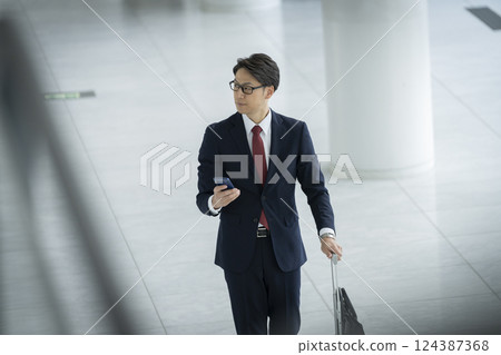 一位 40 多歲的商人拿著智慧型手機和行李箱行走 一位 40 多歲的商人拿著智慧型手機和行李箱行走 124387368