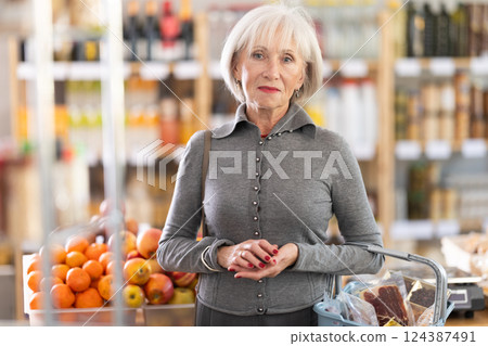 Portrait of mature woman shopper with shopping cart choosing some products in supermarket 124387491