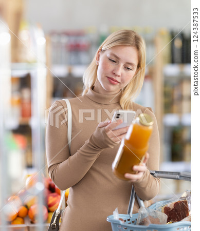 Girl scan QR code, take reading peach juice label using phone camera in shop Girl scan QR code, take reading peach juice label using phone camera in shop 124387533
