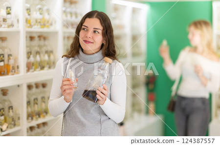 Girl choosing perfume in supermarket while standing near shelves with perfume Girl choosing perfume in supermarket while standing near shelves with perfume 124387557