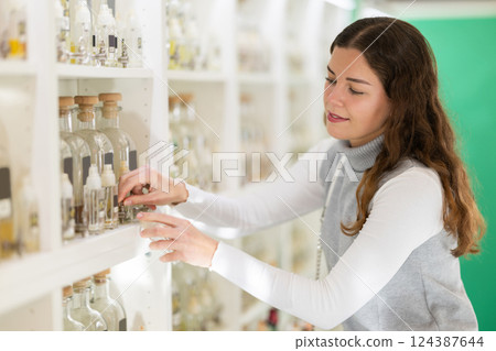 Happy girl chooses perfumes and other perfumery products on shelves of perfume shop Happy girl chooses perfumes and other perfumery products on shelves of perfume shop 124387644