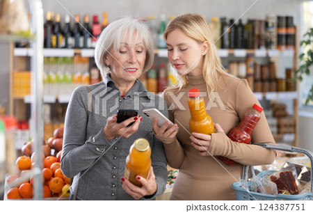 Girl and grandma scan QR code, take reading juice label using phone camera in shop Girl and grandma scan QR code, take reading juice label using phone camera in shop 124387751