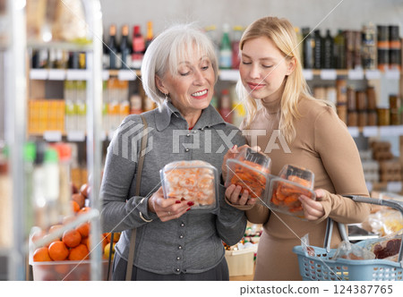 Girl and grandmother buyers examine good, doubt and choose prawn in store Girl and grandmother buyers examine good, doubt and choose prawn in store 124387765