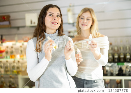 Two girlfriends choose aromatic perfumes together in perfume shop Two girlfriends choose aromatic perfumes together in perfume shop 124387778