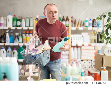 Man with basket of goods looks at display case, looks for household chemistry items Man with basket of goods looks at display case, looks for household chemistry items 124387819