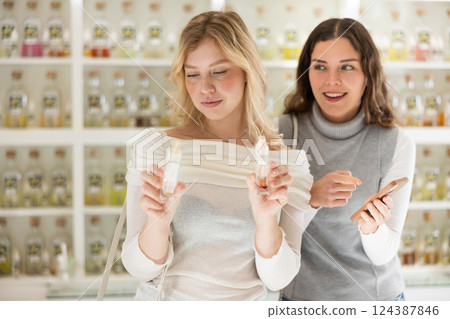 Girl offers her friend to check quality of perfume by scanning QR code with smartphone Girl offers her friend to check quality of perfume by scanning QR code with smartphone 124387846