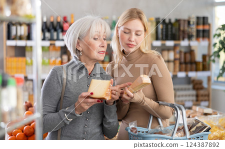 Girl and grandmother buyers examine good, doubt and choose cheese in store 124387892