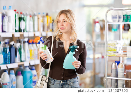 Attentive young girl choosing between two sprays standing between shelves in supermarket 124387893
