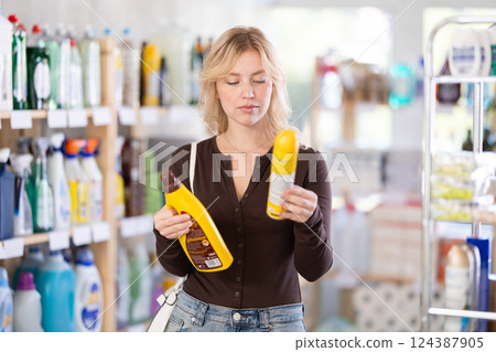 Girl housewife in household store examines goods, chooses liquid furniture polish 124387905