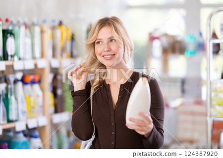 Girl housewife in household store examines goods, chooses hair care product Girl housewife in household store examines goods, chooses hair care product 124387920