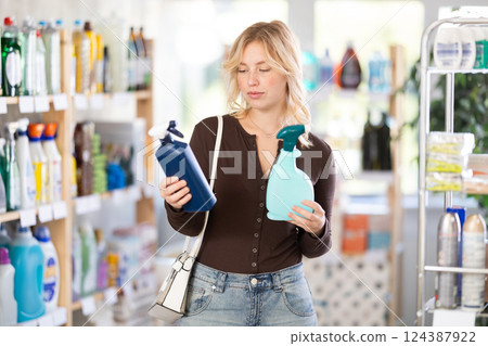 Pretty young woman customer buying spray and choosing between two bottle in store 124387922