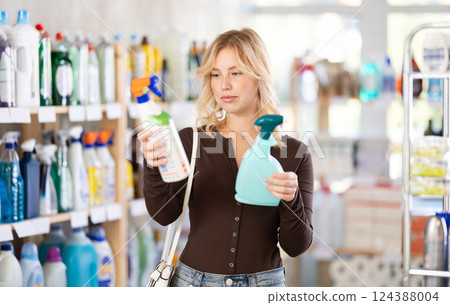 Attentive young girl choosing between two sprays standing between shelves in supermarket Attentive young girl choosing between two sprays standing between shelves in supermarket 124388004
