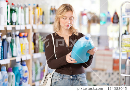Girl housewife in household store examines goods, chooses liquid detergent Girl housewife in household store examines goods, chooses liquid detergent 124388045