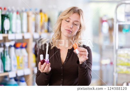 Smiling young woman customer deciding on nail polish in beauty department at store 124388120