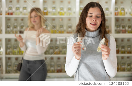 Satisfied young woman chooses and tries perfume in cosmetics store 124388163