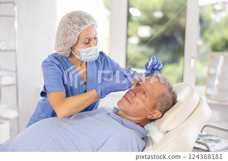 Woman cosmetologist makes injection in forehead of man Woman cosmetologist makes injection in forehead of man 124388181